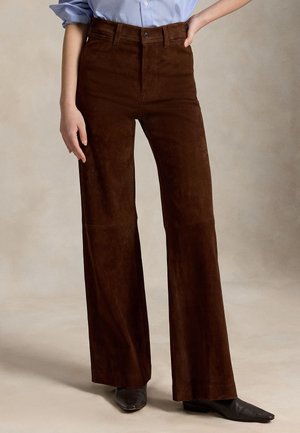 Personne portant un pantalon marron taille haute à jambes larges, associé à des chaussures noires à bout pointu et une chemise bleu clair rentrée.