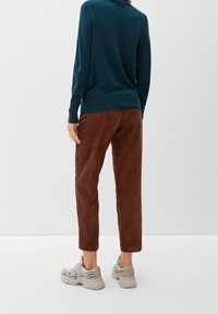Un pull teal à manches longues, un pantalon en velours côtelé marron à rayures verticales, et des baskets gris clair avec des accents noirs.