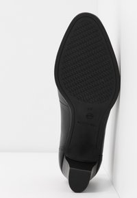 Chaussure en cuir noir avec une semelle en caoutchouc texturée, dotée d'un talon bas et d'un design d'orteil courbé. Taille 37 indiquée sur la semelle.