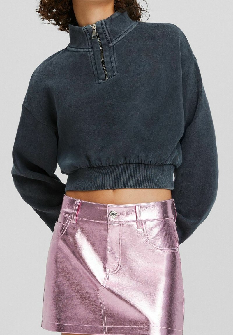 Mörkgrå, kort sweatshirt med hög krage och halvdraret; matchad med en metallisk rosa minikjol som visar en slät, glänsande textur.