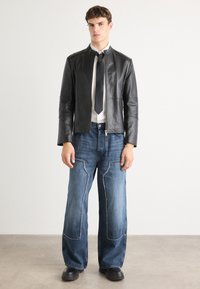 Črna usnjena jakna na zadrgo, bela srajca, črna kravata, široke modre jeanske hlače s detajli patchwork in črna obutev. Minimalistična estetika.