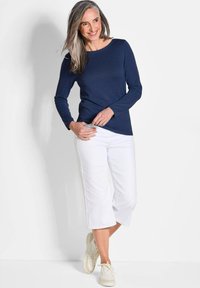 Langärmliges navy Oberteil kombiniert mit weißen Cropped-Hosen und cremefarbenen Sneakers. Glatter Stoff, schlichtes Design und entspannte Passform.