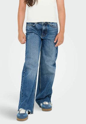 Blue denim wide-leg jeans with a faded wash, frayed hem, and five-pocket design, paired with blue sneakers and a white tank top.