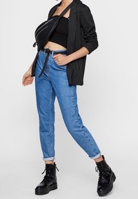 Černý oblekový blejzr s jemným proužkem přes černý crop top, doplněný o světlé modré zúžené džíny a černé boty s tkaničkami na silné podrážce.