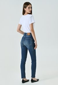 Jeans scuri a vita alta in denim, con un design per tasche posteriori e un'etichetta in pelle marrone, abbinati a una maglietta bianca e ballerine nere.