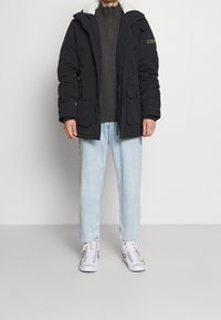 Námořnická pufovaná bunda s kapucí, s límcem z beránka, dvěma předními kapsami a zapínáním na knoflíky, spárovaná se světle modrými džínami a bílými teniskami.