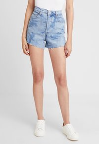 High-waisted denim shorts in light blue with a faded camo pattern, frayed hem, and five-pocket design. Worn with white sneakers.