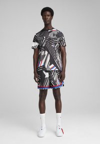 Czarny i biały zestaw sportowy w geometryczne wzory. Koszulka z krótkim rękawem oraz szorty z niebieskimi i czerwonymi akcentami. Białe sneakersy.