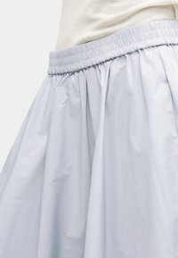 Ανοιχτό γκρι φούστα με ελαστική τσιμπημένη μέση φορεμένη πάνω από μπεζ τοπ, που δείχνει την υφή του υφάσματος και τις ρυτίδες στο φυσικό φως.