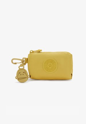 Pochette jaune zippée en matériau lisse, avec un logo circulaire et un porte-clés en forme de singe attaché en décoration.