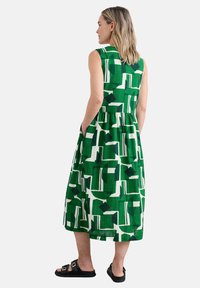 Grünes Kleid mit geometrischem Muster in Weiß und Dunkelblau. Ärmelloses Design mit gerafftem Taillenbund und seitlichen Taschen.