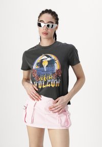 Camiseta gráfica gris con un diseño colorido que presenta palmeras y flores, combinada con una minifalda cargo rosa claro con bolsillos laterales.