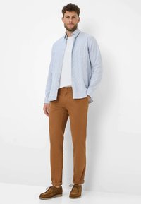 Camicia button-up a righe azzurre e bianche sopra una maglietta bianca, abbinata a pantaloni marroni e scarpe stringate marroni.