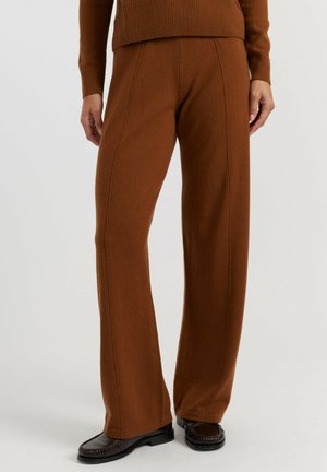 Pantalon en maille marron à jambes larges porté avec des mocassins noirs, montrant les détails des coutures le long des jambes et un ourlet côtelé à la taille.