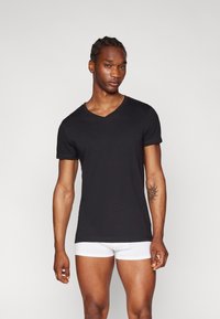 Black short-sleeve v-neck t-shirt made of soft cotton. Features a fitted design with rolled sleeves, worn with white boxer briefs.