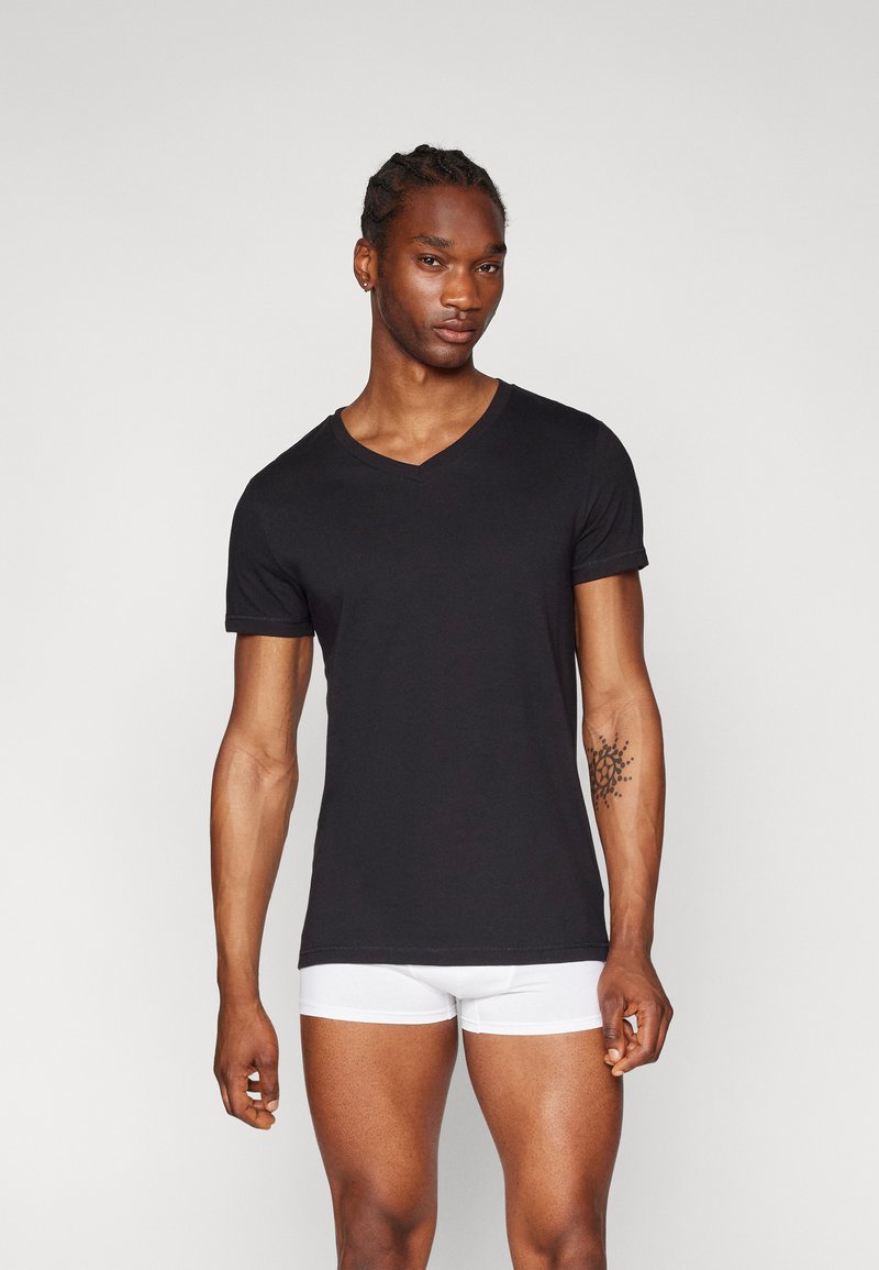 Schwarzes kurzärmliges V-Ausschnitt-T-Shirt aus weicher Baumwolle. Hat ein eng anliegendes Design mit umgeschlagenen Ärmeln und wird mit weißen Boxer-Shorts getragen.