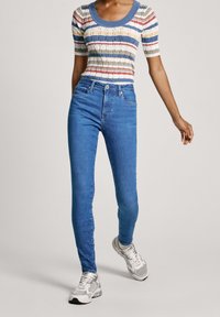 Jeans ajustados de talle alto en azul combinados con una blusa de punto de canalé de rayas multicolores. La tela parece suave con un diseño texturizado.