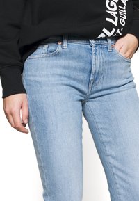 Jasnoniebieskie dżinsy skinny o wysokim stanie, z delikatnym wyblaknięciem, pięcioma kieszeniami i mosiężnymi akcentami. Połączone z czarną bluzą.