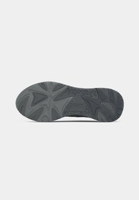 Suela de zapato de goma negra con un diseño texturizado, que presenta patrones geométricos y un logotipo. Perfil plano con elementos de tracción pronunciados.