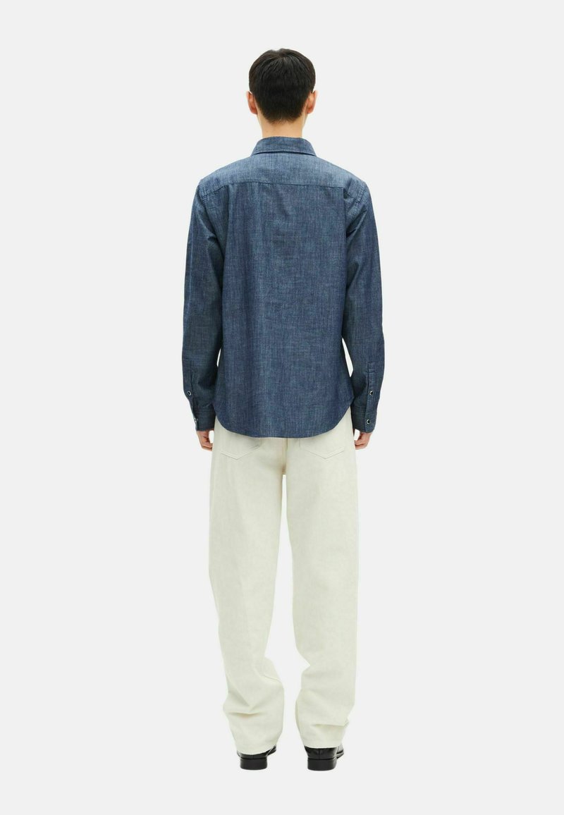 Jeansskjorta i mörkblått, långärmad, med knäppta manschetter och klassisk krage, tillsammans med lösa vita byxor och svarta skor.