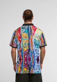 Barvna polo majica z živahnim vzorcem spirala in geometrijskih oblik v rdeči, modri, rumeni in zeleni barvi, z črnim ovratnikom.