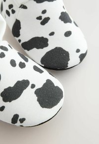 Zapatos slip-on de patentes en blanco y negro con un upper de tela suave que presenta manchas abstractas similares a las de una vaca y un diseño de punta redonda.