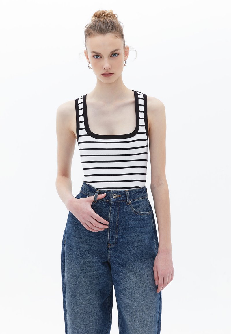 Body a righe bianco e nero con scollatura quadrata, abbinato a jeans di jeans blu a vita alta. Il tessuto è a coste con bordi a contrasto audaci.