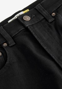Schwarze Denim-Jeans mit slim Fit, Metallknopf-Beschlägen und gestickten Details entlang des Taillenbands und der Taschen.