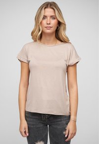 T-shirt à manches courtes, beige clair, avec un col rond, une texture douce et des manches retroussées, associé à un jean foncé déchiré.