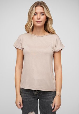 T-shirt à manches courtes, beige clair, avec un col rond, une texture douce et des manches retroussées, associé à un jean foncé déchiré.