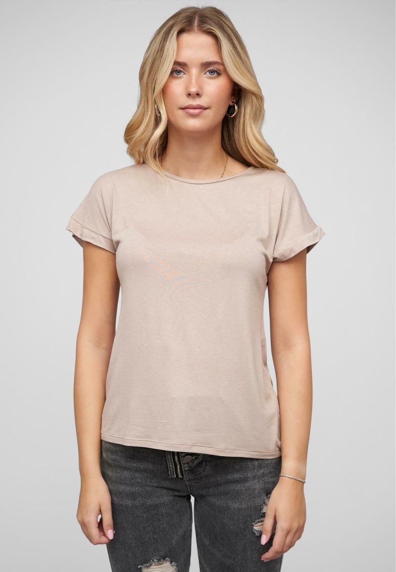 T-shirt à manches courtes, beige clair, avec un col rond, une texture douce et des manches retroussées, associé à un jean foncé déchiré.