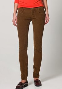 Bruine corduroy skinny jeans met een gladde textuur, vijf zakken en een knoopsluiting, gecombineerd met donkere loafers.