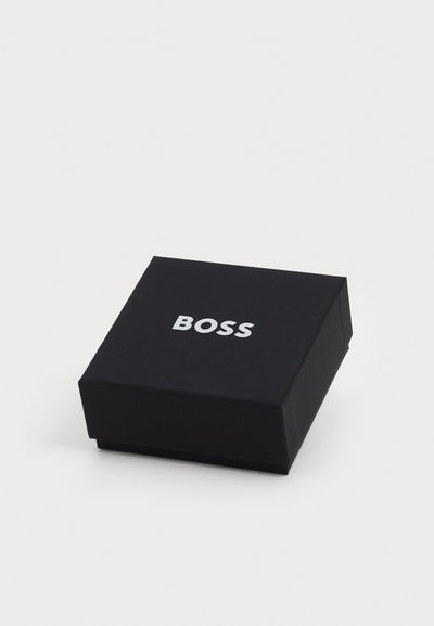 Черен квадратен кутия с гладка текстура и капак, с думата "BOSS" в удебелен, сребърен шрифт на горната повърхност.
