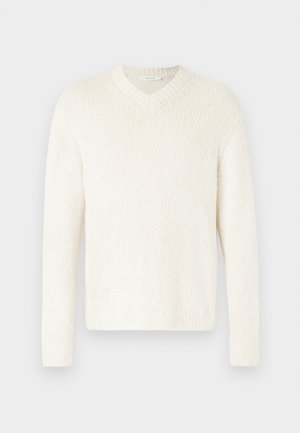 V-nyakú pulóver világos krém színben, textúrált kötésből. Hosszú ujjak, laza fazon, bordás mandzsetták és szegély. Egyszerű dizájn, további díszítések nélkül.