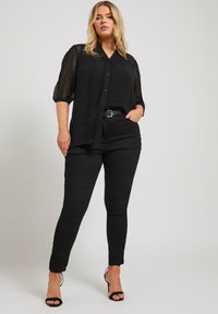 Svart genomskinlig blus med texturerade detaljer, knäppning fram och trekvartsärmar, i kombination med svarta figurnära byxor och klacksandaler.