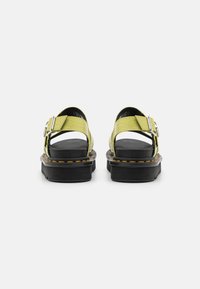 Sandalias negras con un upper texturizado en verde lima, hebilla ajustable y costuras amarillas en una suela negra gruesa, con un diseño de parte trasera abierta.
