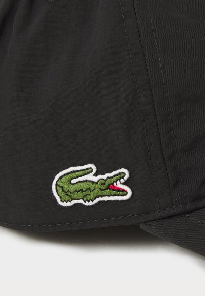 Casquette noire avec un logo de crocodile brodé vert et des accents rouges, sur fond de tissu lisse.