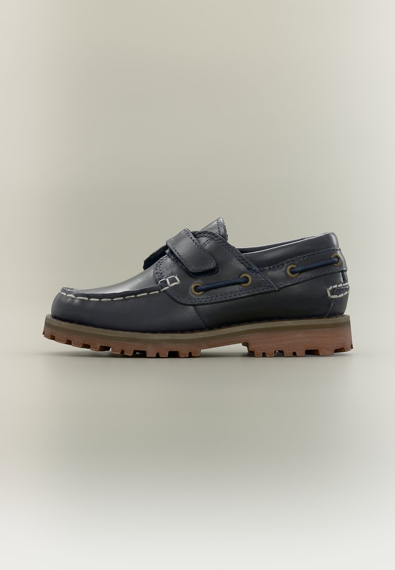 Σκούρο μπλε δερμάτινο παπούτσι σκαφού με λευκή ραφή, λουρί Velcro, καφέ ανθεκτική σόλα και λεπτομέρεια με μπλε κορδόνι σε ουδέτερο φόντο.
