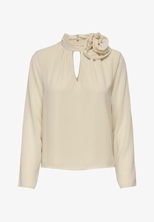 Cremefarbene Bluse mit langen Ärmeln, hohem Kragen, Schlitz am Ausschnitt und großem Stoffblumen-Detail auf der linken Schulter.