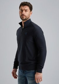 Maglione zip-up blu con alto colletto e polsini a costine, realizzato in materiale morbido. Presenta una piccola etichetta con logo sul petto.