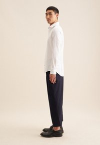 Witte lange mouw shirt met manchetten, donkere broek en zwarte schoenen. Het shirt heeft een klassieke kraag en een licht gebogen zoom.