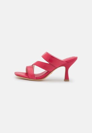 Sandale à talon haut rouge avec trois larges brides et un talon fin et courbé sur fond blanc.