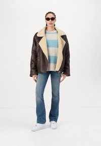 Brown leather jacket with a cream shearling collar, blue and beige striped sweater, light blue jeans, and white sneakers. Sunglasses included.