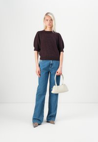 Burgundy knit sweater with puff sleeves, paired with high-waisted blue flared jeans. Model holds a small white handbag and wears beige heels.