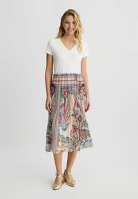 Robe à col en V avec un haut blanc et une jupe fluide à motifs, comportant des designs floraux et paisley dans des tons de rose, vert et bleu.