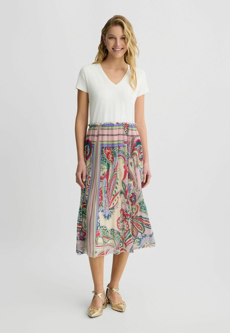 Robe à col en V avec un haut blanc et une jupe fluide à motifs, comportant des designs floraux et paisley dans des tons de rose, vert et bleu.