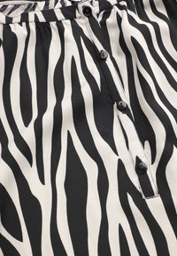 Zebrapatroon stof met zwarte en witte golvende lijnen, voorzien van een voorknopsluiting en zwarte plastic knopen op een gladde textuur.