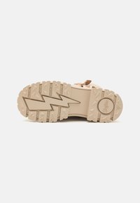 Shoe sole featuring a rugged, light beige design with a zigzag tread pattern and a circular logo, providing traction and durability.
