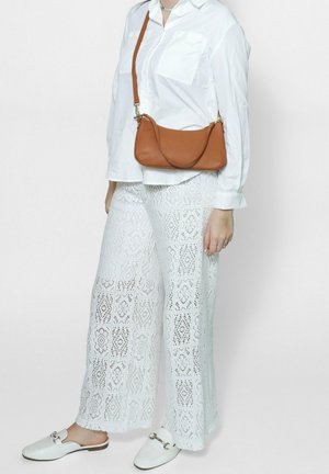 Witte kanten wijde broek met geometrische patronen, gecombineerd met een lange mouwen witte blouse met knoopjes en een bruine leren schoudertas. Witte instap schoenen.