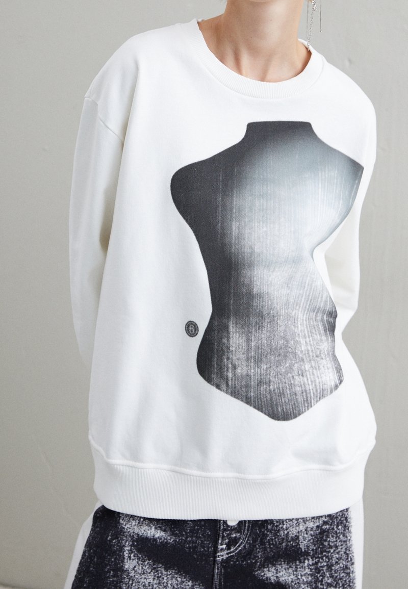Vit sweatshirt med en stor, abstrakt svart och grå torso grafik. Mjuk textur med ribbade ärmslut och nederkant, designad för en avslappnad passform.